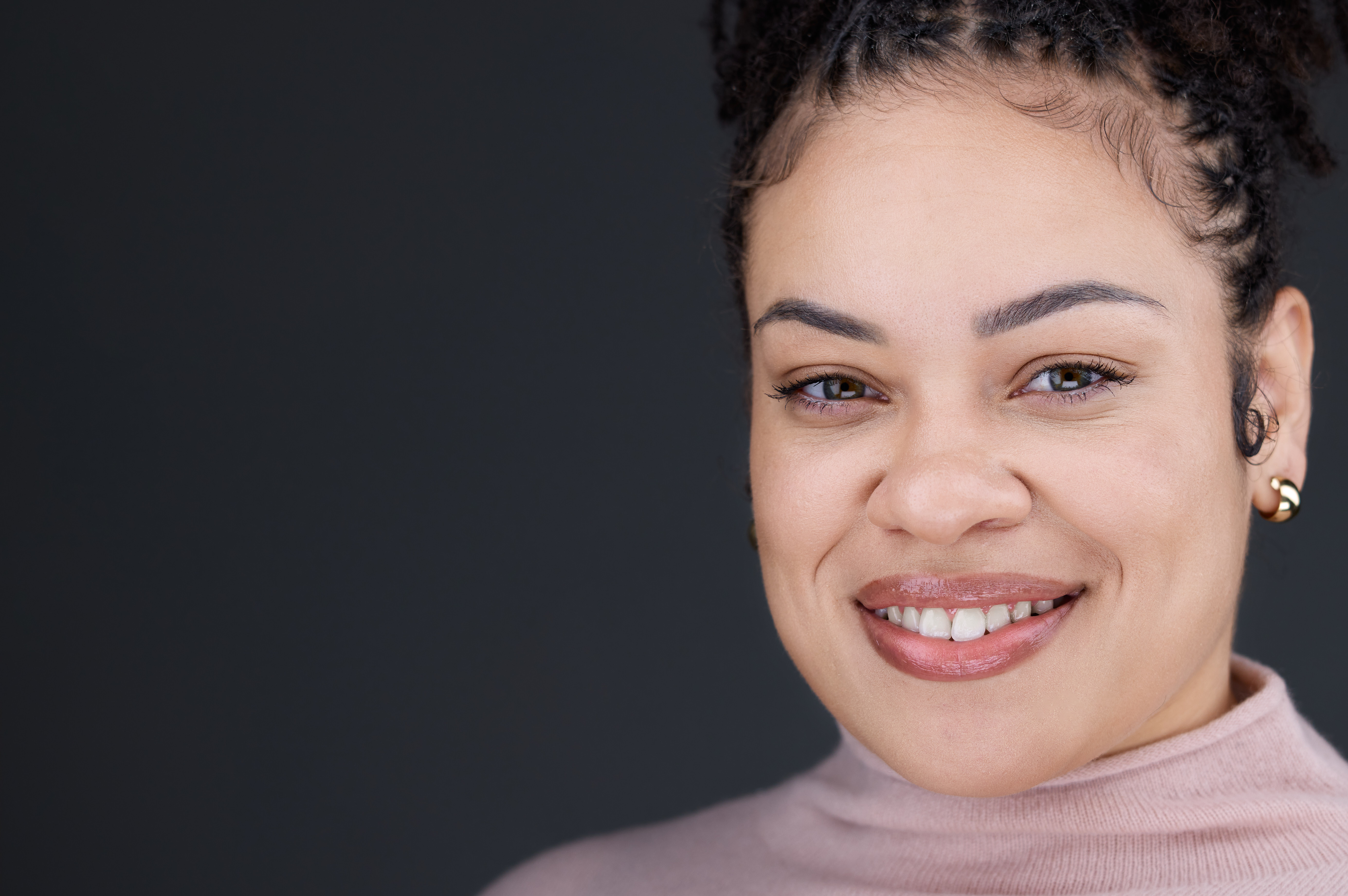 Alia Gaddy smiling and wearing a pink blouse, facing the camera with a friendly and approachable expression. The background is softly blurred, suggesting an indoor setting with warm lighting, creating a welcoming and positive atmosphere.